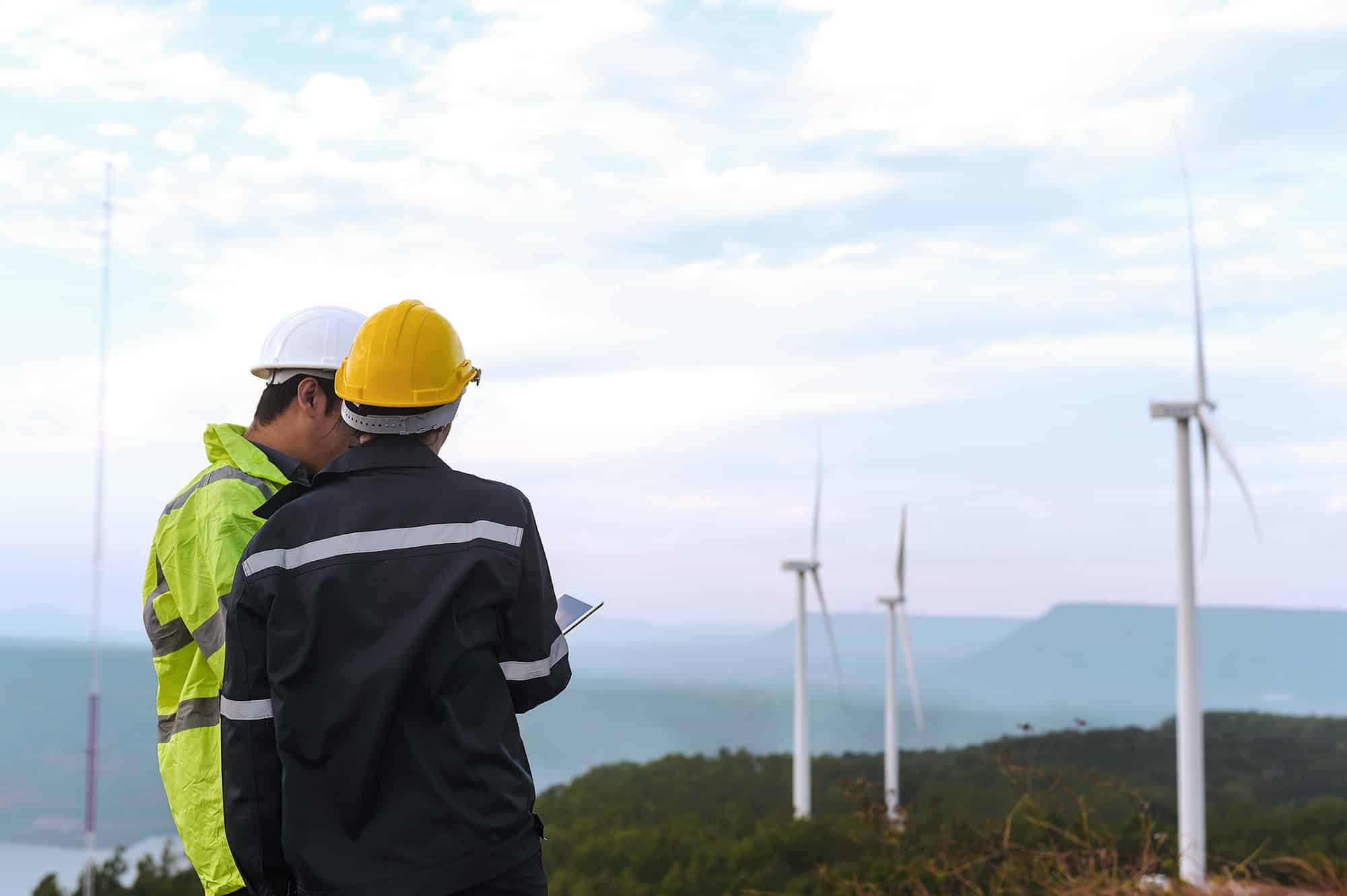 Outsourcing to sub-suppliers can be beneficial. Here are two construction workers in front of some wind turbines.